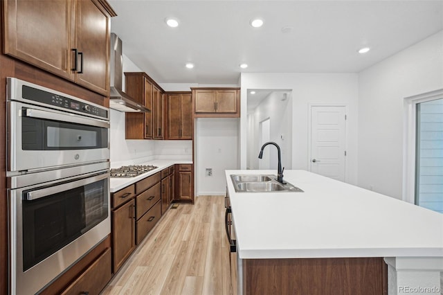 2102 Wagon Wheel Aly, Brighton, CO 80601 - kitchen featuring stainless steel appliances, wall chimney range hood, light wood-style flooring, a kitchen island with sink, and recessed lighting