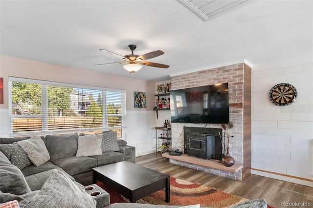 living room with a ceiling fan, a wood stove, plenty of natural light, and wood finished floors