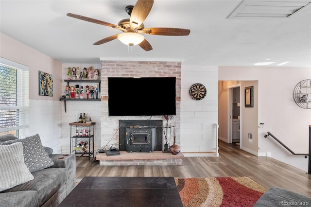 living room with wood finished floors, visible vents, baseboards, a ceiling fan, and a wood stove