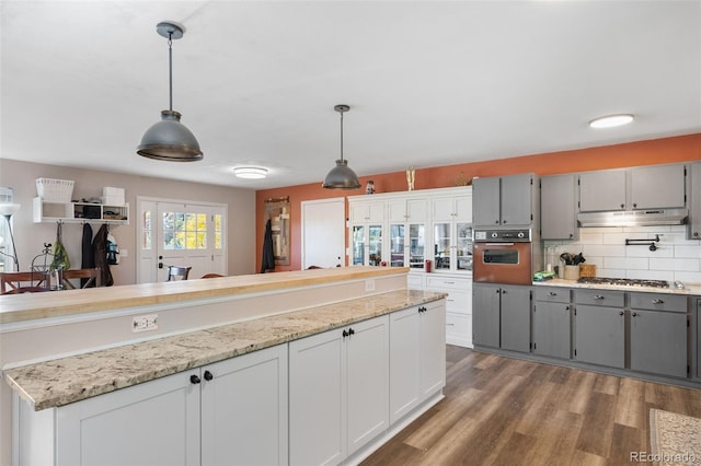 kitchen featuring wall oven, decorative backsplash, wood finished floors, gray cabinets, and under cabinet range hood