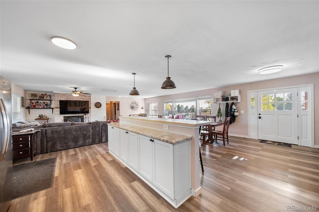 kitchen with light wood-type flooring, white cabinetry, pendant lighting, and light stone counters