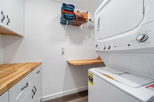 clothes washing area featuring stacked washing maching and dryer, baseboards, dark wood finished floors, and cabinet space