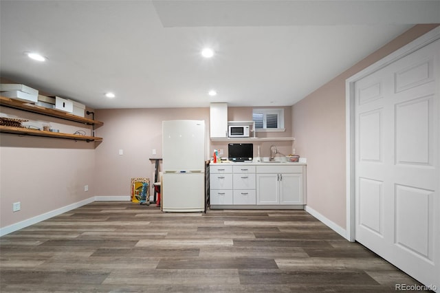 kitchen with wood finished floors, white appliances, a sink, and white cabinetry