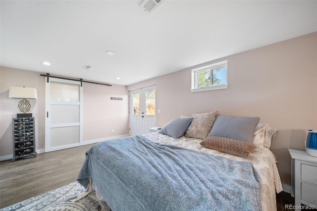 bedroom featuring a barn door, baseboards, visible vents, wood finished floors, and recessed lighting