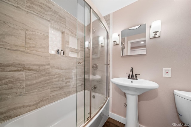 full bathroom featuring bath / shower combo with glass door, a sink, toilet, and baseboards