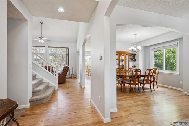foyer with arched walkways, a textured ceiling, ceiling fan with notable chandelier, baseboards, and light wood-type flooring