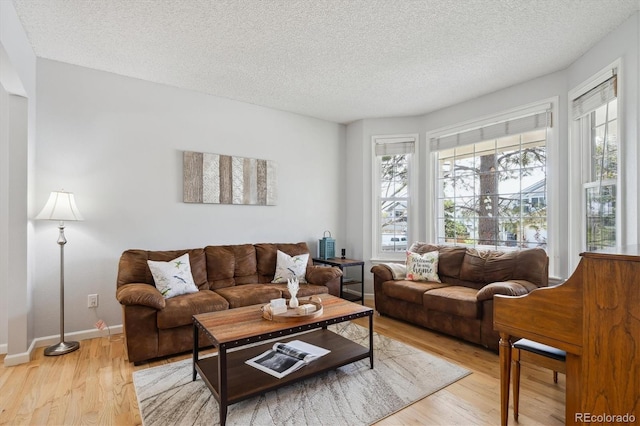 living area featuring light wood-style floors, baseboards, a textured ceiling, and a wealth of natural light