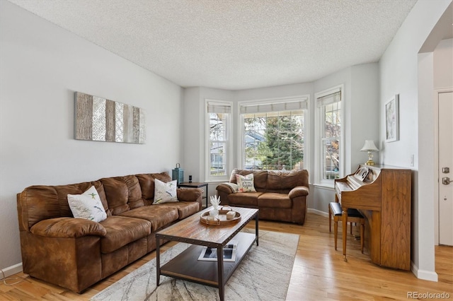 living area featuring light wood-style floors, arched walkways, a textured ceiling, and baseboards