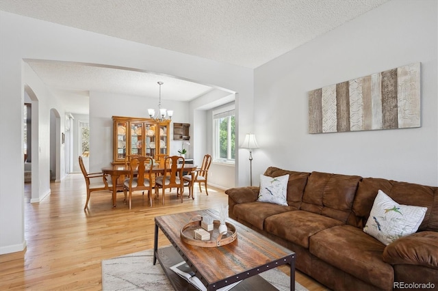 living room featuring light wood-style floors, arched walkways, baseboards, and a chandelier