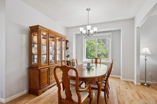 dining area featuring a textured ceiling, a notable chandelier, baseboards, and light wood finished floors