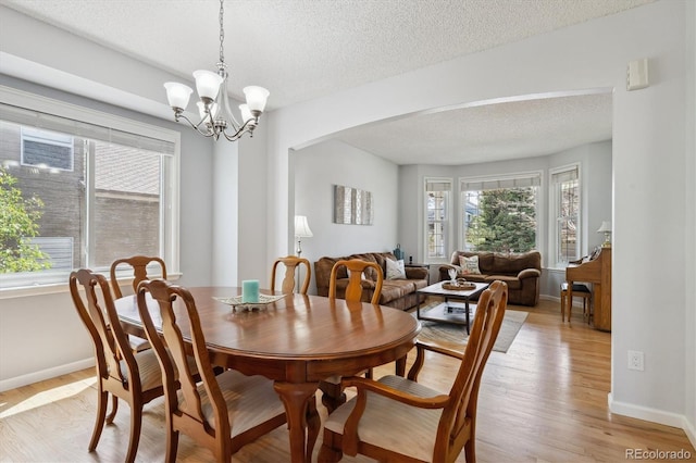 dining room featuring baseboards, light wood-style flooring, a textured ceiling, and arched walkways