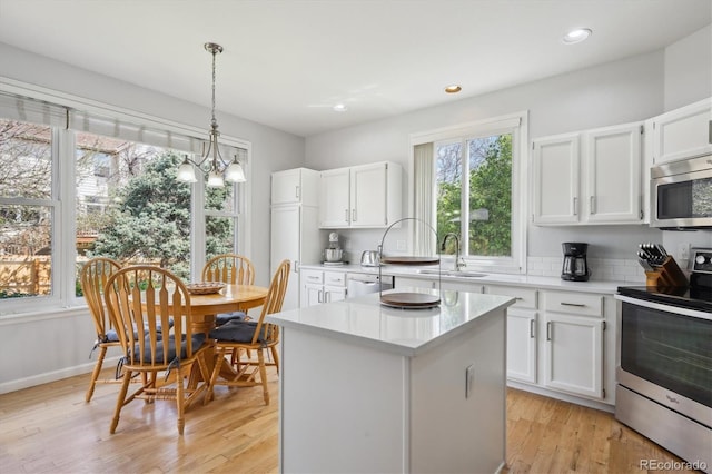 kitchen with white cabinets, a sink, light countertops, stainless steel appliances, and a kitchen island