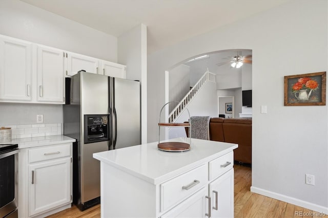 kitchen featuring ceiling fan, stainless steel fridge, light wood-type flooring, white cabinets, and arched walkways