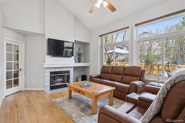 living area featuring ceiling fan, light wood finished floors, a fireplace, high vaulted ceiling, and baseboards