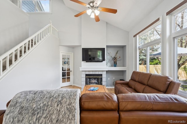 living room with ceiling fan, wood finished floors, a tile fireplace, high vaulted ceiling, and stairs
