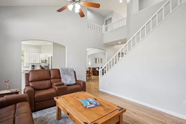 living area with stairway, arched walkways, a ceiling fan, and light wood finished floors