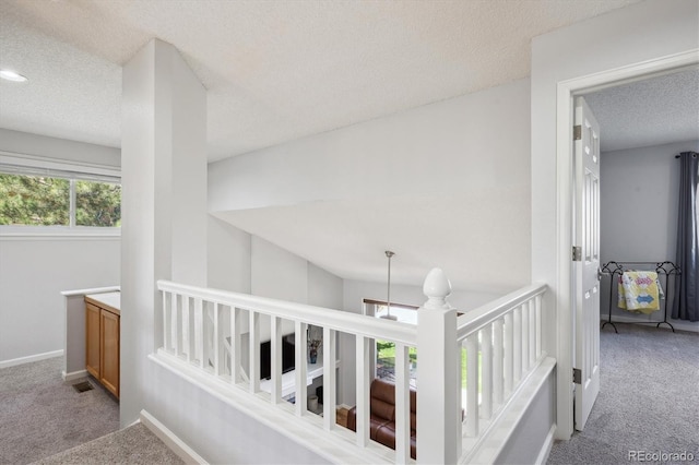 corridor featuring visible vents, baseboards, a textured ceiling, carpet flooring, and an upstairs landing