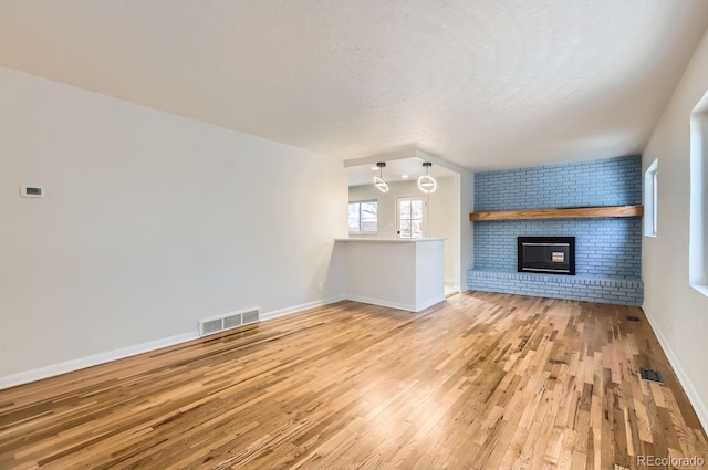 unfurnished living room with light hardwood / wood-style flooring, a fireplace, a textured ceiling, and brick wall