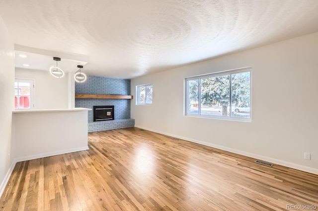 unfurnished living room featuring wood-type flooring, a textured ceiling, a brick fireplace, and a wealth of natural light