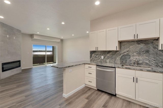 kitchen featuring a peninsula, a fireplace, white cabinetry, and dishwasher