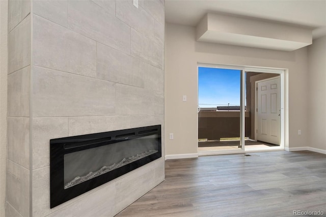 interior space featuring a tile fireplace, visible vents, baseboards, and wood finished floors