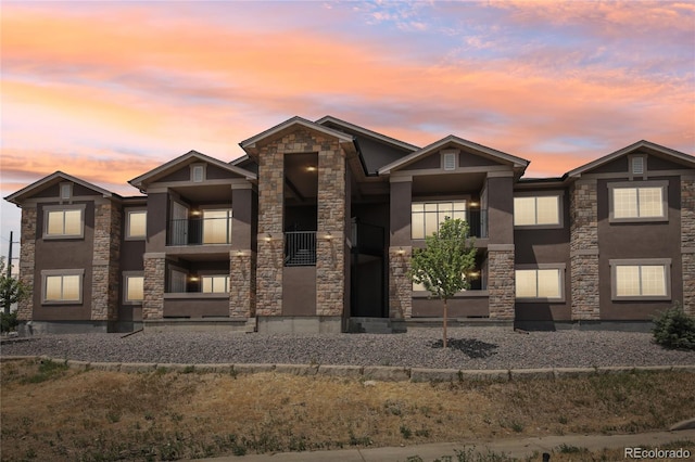 view of front facade featuring stone siding, a balcony, and stucco siding