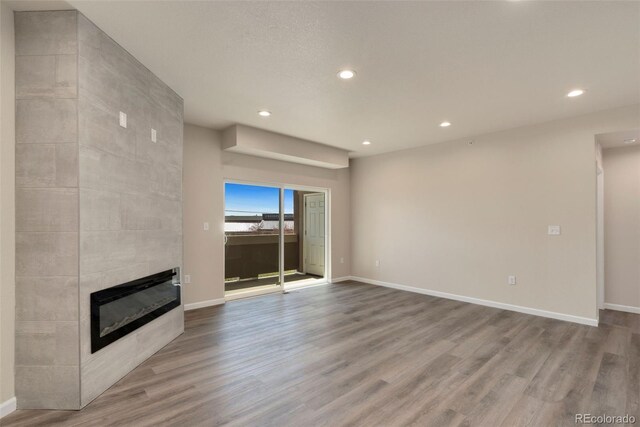 unfurnished living room with a tile fireplace, baseboards, and wood finished floors