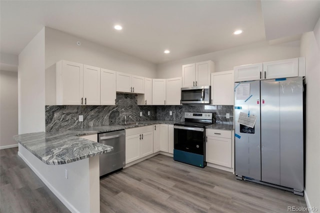 kitchen with dark stone counters, appliances with stainless steel finishes, a peninsula, light wood-style floors, and white cabinetry