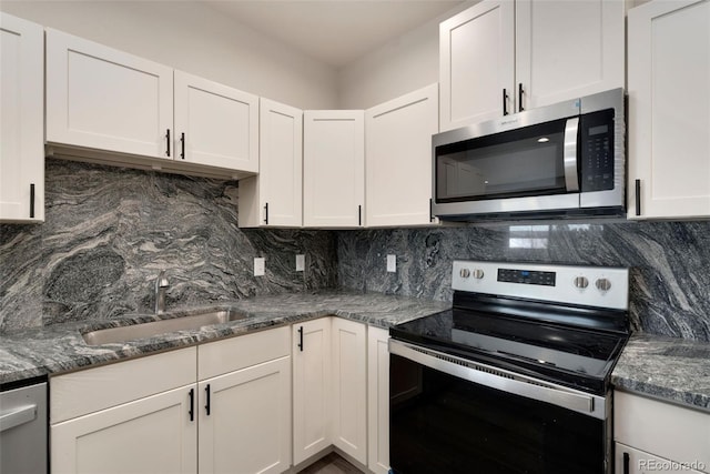 kitchen featuring stainless steel appliances, a sink, white cabinetry, dark stone counters, and tasteful backsplash