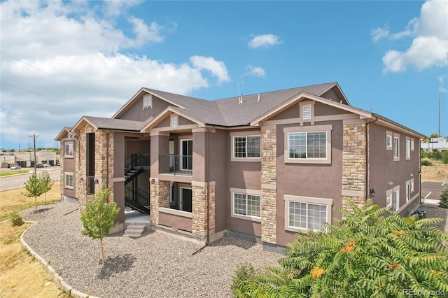 exterior space featuring stone siding, a balcony, and stucco siding