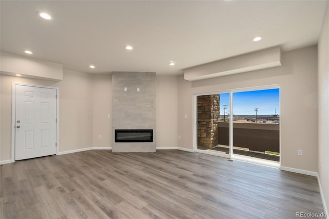 unfurnished living room with recessed lighting, baseboards, a tiled fireplace, and wood finished floors