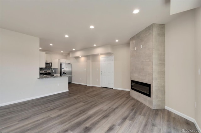 unfurnished living room featuring a tile fireplace, recessed lighting, baseboards, and wood finished floors