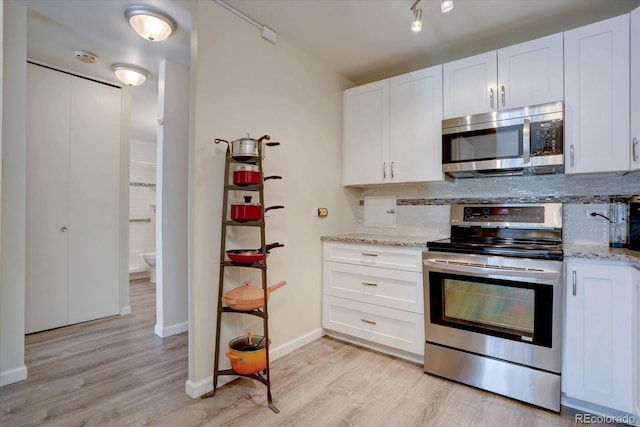 kitchen featuring light stone counters, stainless steel appliances, white cabinets, light wood-style floors, and tasteful backsplash