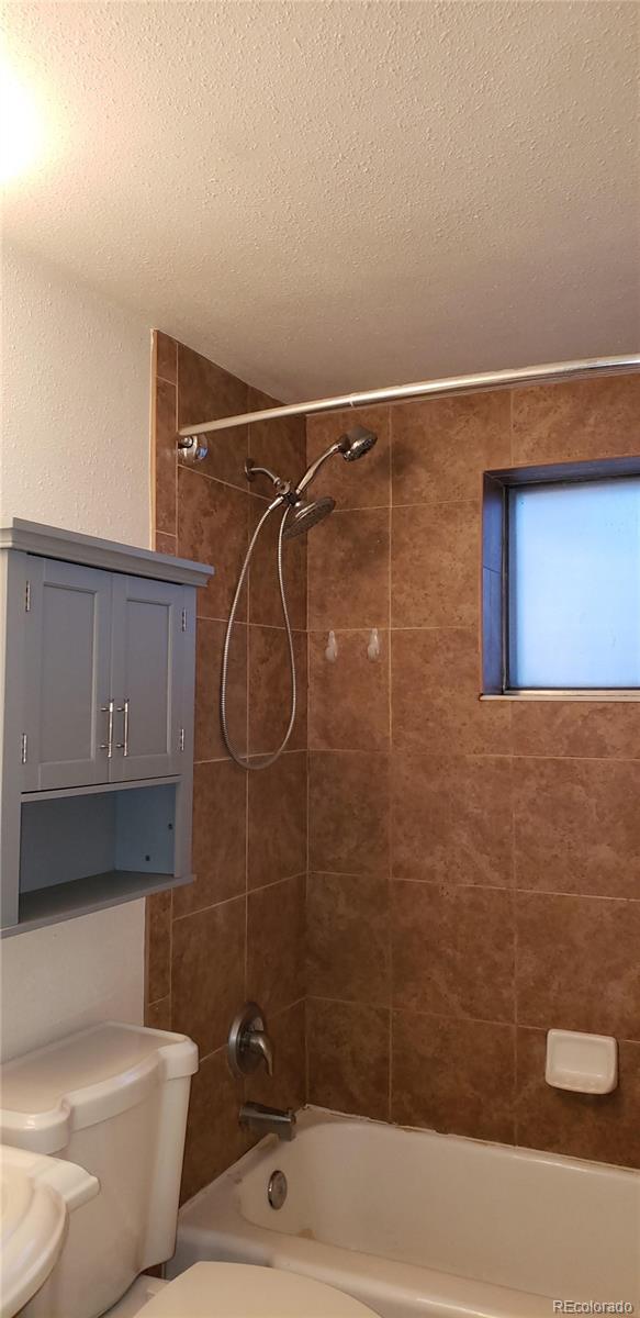 full bathroom featuring washtub / shower combination, toilet, and a textured ceiling