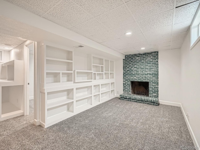 basement featuring built in shelves, a brick fireplace, and carpet flooring