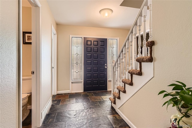 foyer entrance with stone tile flooring, stairway, and baseboards