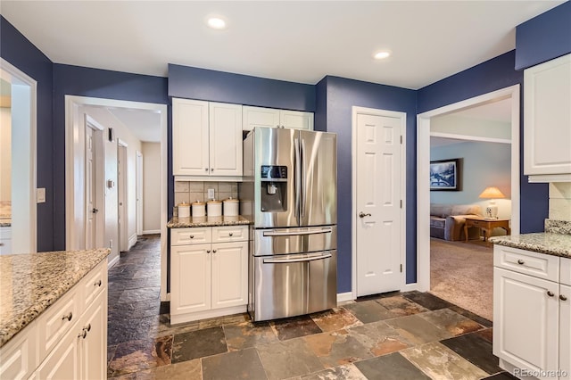 kitchen with stainless steel fridge, backsplash, white cabinets, stone tile flooring, and light stone countertops