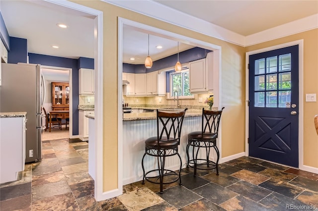 kitchen featuring stone tile flooring, freestanding refrigerator, white cabinets, backsplash, and recessed lighting