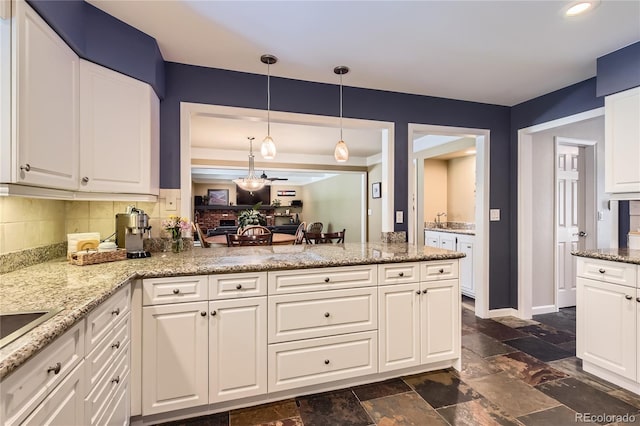 kitchen featuring backsplash, stone tile floors, white cabinetry, light stone counters, and pendant lighting