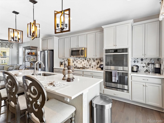 kitchen with stainless steel appliances, a sink, light countertops, backsplash, and dark wood-style flooring