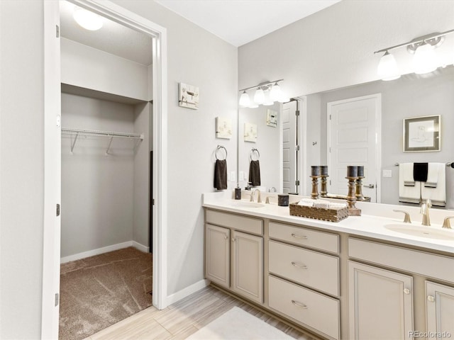 bathroom with double vanity, a walk in closet, and baseboards
