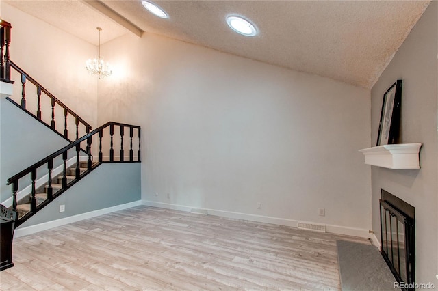 unfurnished living room with a notable chandelier, lofted ceiling, a textured ceiling, and light hardwood / wood-style flooring