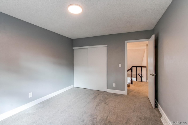 unfurnished bedroom featuring a textured ceiling, light colored carpet, and a closet