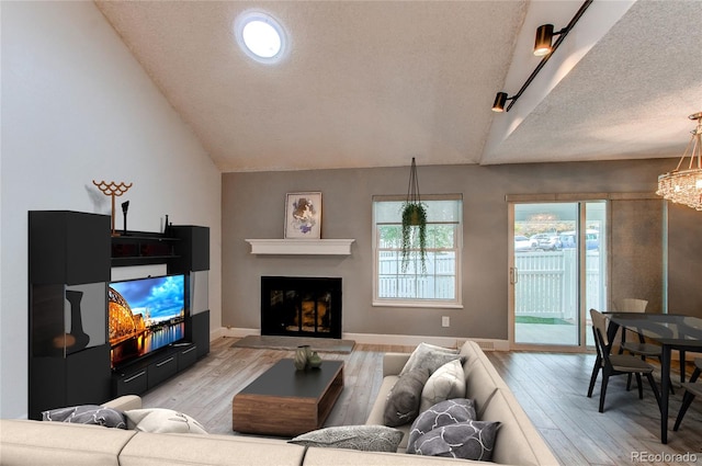 2790 S Wheeling Way, Aurora, CO 80014 - living area featuring vaulted ceiling, light wood-style flooring, a textured ceiling, a fireplace with raised hearth, and a chandelier