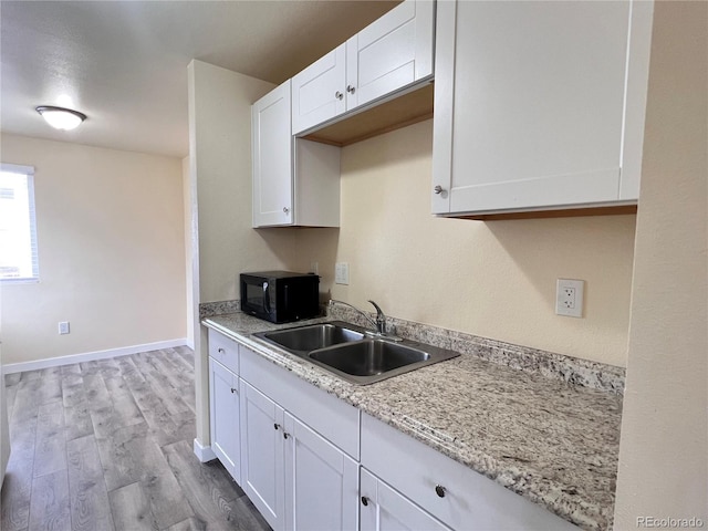 kitchen featuring white cabinets, light hardwood / wood-style floors, light stone counters, and sink