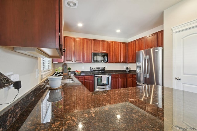 kitchen featuring appliances with stainless steel finishes, kitchen peninsula, dark stone countertops, and sink