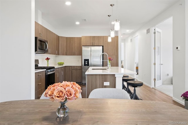 kitchen featuring appliances with stainless steel finishes, a kitchen bar, pendant lighting, light hardwood / wood-style floors, and sink