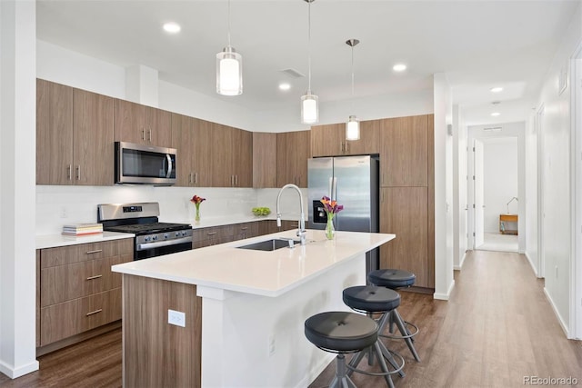 kitchen with an island with sink, appliances with stainless steel finishes, a kitchen breakfast bar, hardwood / wood-style flooring, and pendant lighting