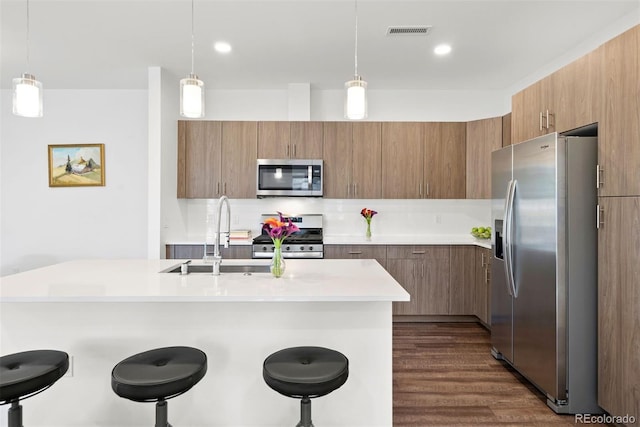 kitchen featuring dark wood-type flooring, hanging light fixtures, stainless steel appliances, sink, and a breakfast bar