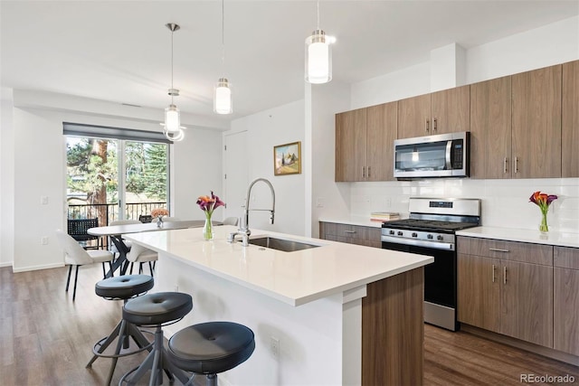 kitchen with appliances with stainless steel finishes, sink, pendant lighting, and a center island with sink